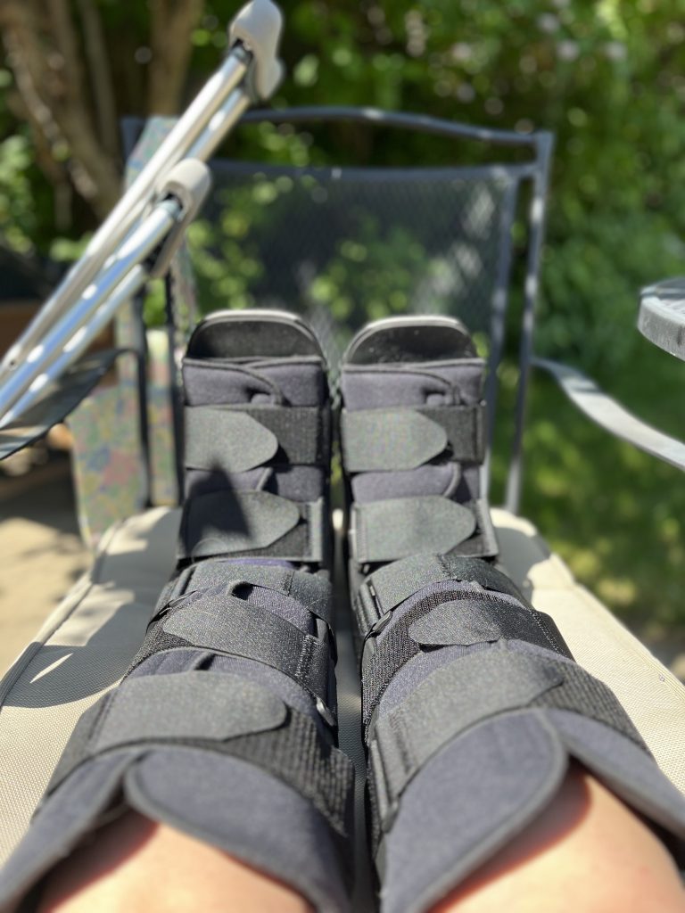 Feet encased in boots propped on a chair, with crutches nearby